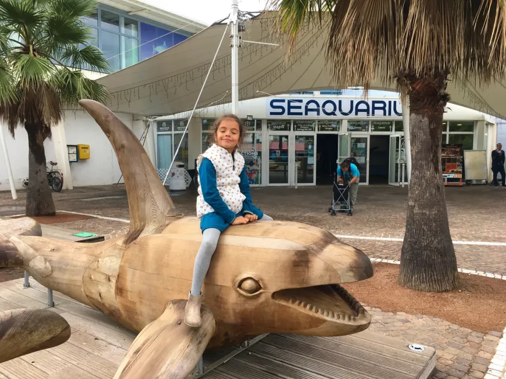 Photo par diegoenfrance.com : fille souriant sur une sculpture de dauphin devant le Seaquarium au Grau-du-Roi.