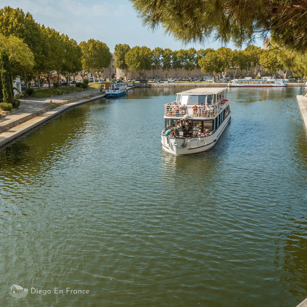 Barque touristique naviguant sur le canal qui longe les remparts d’Aigues-Mortes. Photographie de diegoenfrance.com