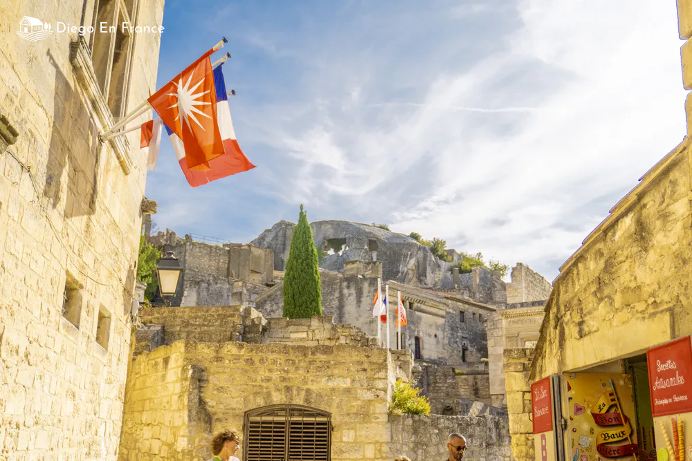 Fotografía de diegoenfrance.com de calle de piedra con banderas provenzales frente a las ruinas del castillo de Les Baux