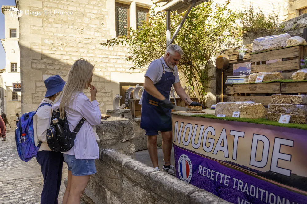 Fotografía de diegoenfrance.com de un vendedor cortando nougat mientras turistas prueban este dulce provenzal en Les Baux