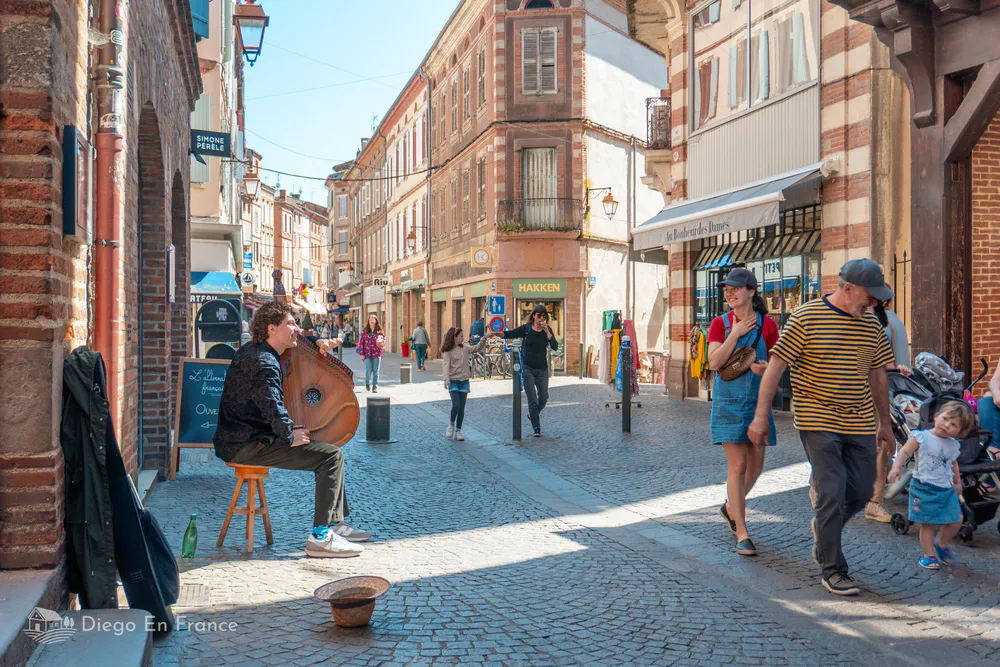 Musicien jouant dans les rues piétonnes d'Albi, créant l'ambiance des promenades dans la vieille ville.