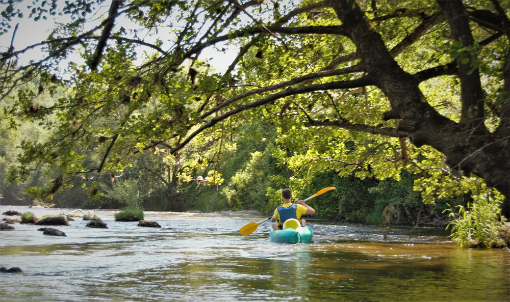 Person paddling a kayak on the river near the village, outdoor adventure in the southwest of France.