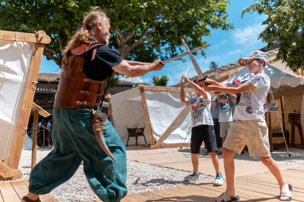 Niños jugando a luchar con espadas en el campamento medieval de Carcasona, entretenimiento histórico en familia