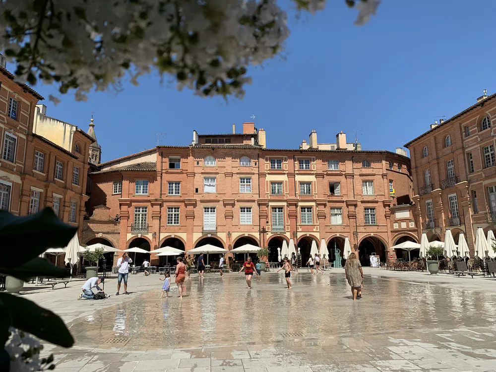 View of the Place Nationale in Montauban, surrounded by arcades and brick buildings, ideal for a cultural getaway from Toulouse.