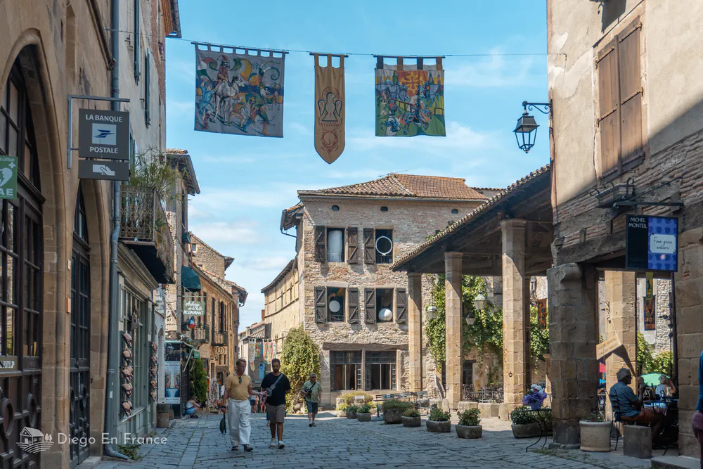 View of the main square of Cordes-sur-Ciel with its covered market and medieval banners, one of the most charming villages to visit from Toulouse. Photo by diegoenfrance.com
