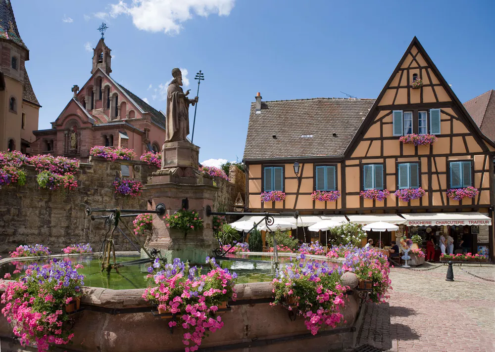 A fountain with flowers and half-timbered houses in Eguisheim, one of the most beautiful villages in France.