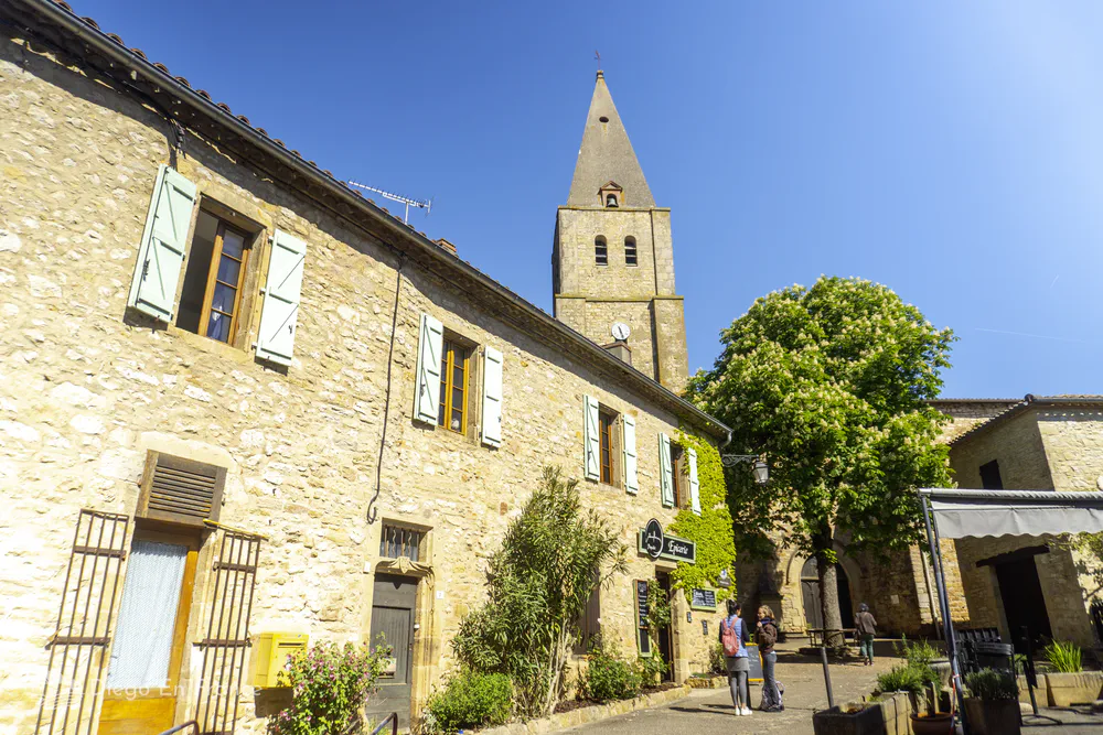 View of the Saint-Corneille church tower from the central square of Puycelsi, with its cozy atmosphere and typical architecture.