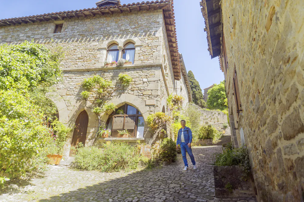 A traveler walking through a golden-stone medieval street in Bruniquel, Occitanie.
