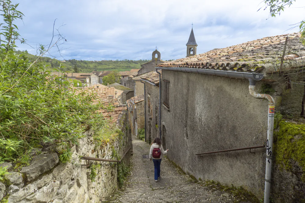 Visitante descendiendo una calle medieval con vistas a los tejados y la iglesia del pueblo.