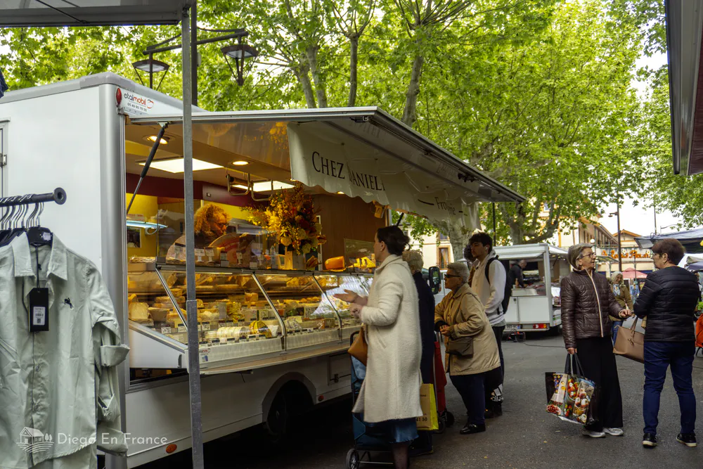 Weekly market in Saint-Sulpice-la-Pointe with sellers and buyers in a shady setting.