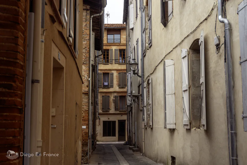 Narrow pedestrian passageway with old facades and wooden shutters in Lavaur.