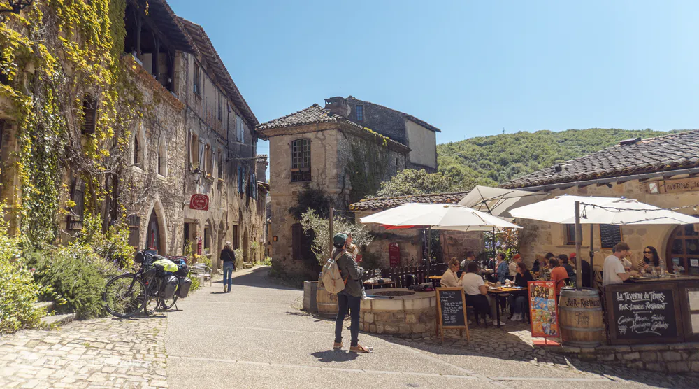 People enjoying a meal on a terrace in Bruniquel’s village center surrounded by stone buildings.