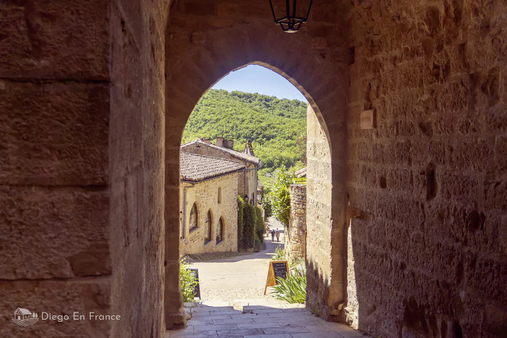 View through a medieval arch in Bruniquel showing rooftops and the Occitan countryside beyond.